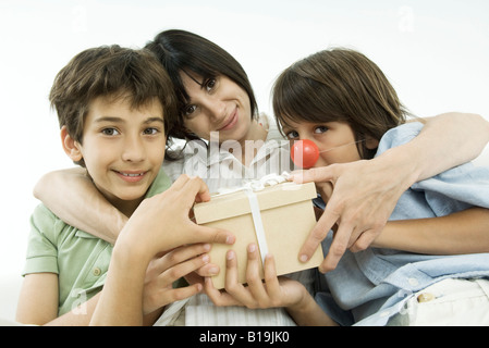 Madre seduta con due figli, tenendo dono, sorridente in telecamera Foto Stock