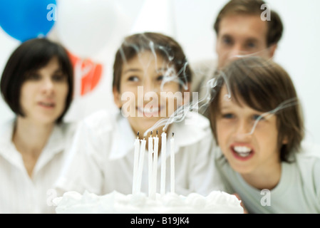 Ragazzi soffiando le candeline sulla torta di compleanno e i genitori in background Foto Stock