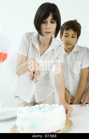 Donna taglio torta di compleanno, figlio guardando Foto Stock