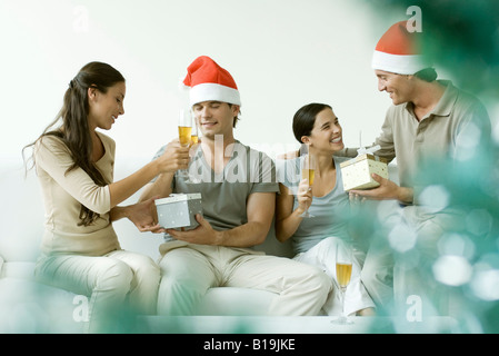 Due coppie lo scambio di regali di Natale, bevendo champagne, uomini che indossano cappelli di Babbo Natale Foto Stock