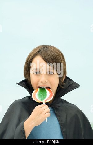 Ragazzo che indossa vampire cape, mangiando grandi lecca-lecca, ritratto Foto Stock
