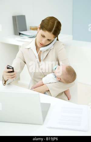 Lavoro giovane azienda madre baby, parlando al telefono fisso e guardando il telefono cellulare Foto Stock