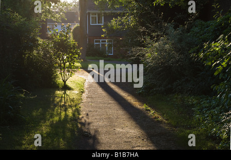 La mattina presto luce bassa gettando ombre su un asfalto sentiero tra case su un moderno complesso residenziale Foto Stock