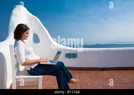 Giovane donna writting sul suo laptop macbook in una terrazza mediterranea in Casapueblo Punta del Este Uruguay Foto Stock