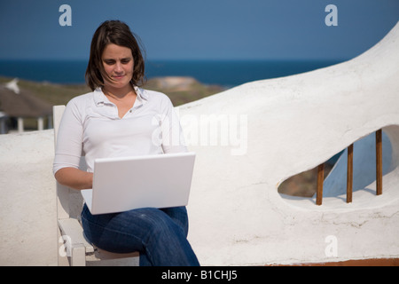 Giovane donna writting sul suo laptop macbook in una terrazza mediterranea in Casapueblo Punta del Este Uruguay Foto Stock