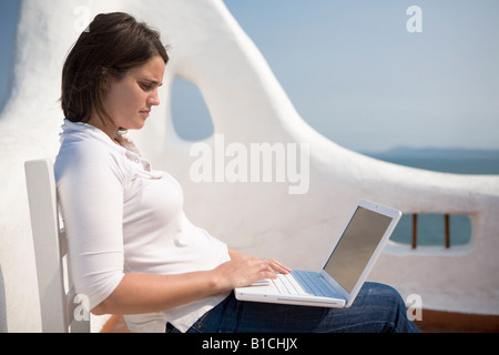 Giovane donna writting sul suo laptop macbook in una terrazza mediterranea in Casapueblo Punta del Este Uruguay Foto Stock