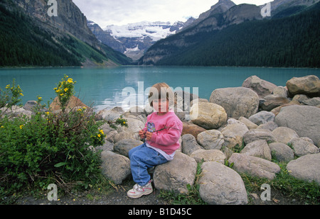 Una giovane ragazza si siede accanto al Lago Louise e il lago è colorata di un azzurro da sedimenti provenienti dai vicini ghiacciai Foto Stock