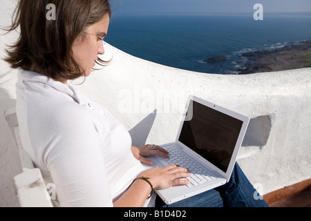 Giovane donna writting sul suo laptop macbook in una terrazza mediterranea in Casapueblo Punta del Este Uruguay Foto Stock