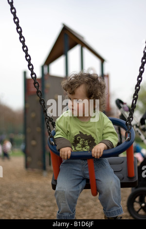 Un bambino piccolo con capelli ricci su altalena nel parco giochi. Foto Stock