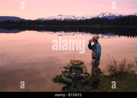 Flyfisherman avente il caffè al mattino sul litorale di McBride lago vicino Lago Morice BC Foto Stock