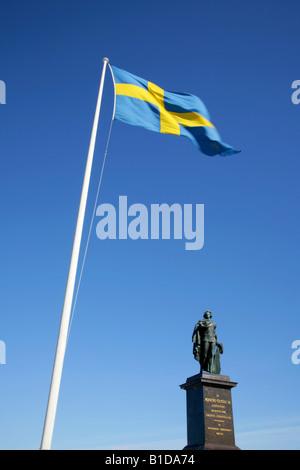 Bandiera svedese in volo la brezza vicino alla statua di Re Gustavo III. Stoccolma, Svezia. Foto Stock