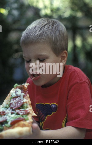 Ragazzo giovane gode di un trancio di pizza con tutto su di esso Foto Stock