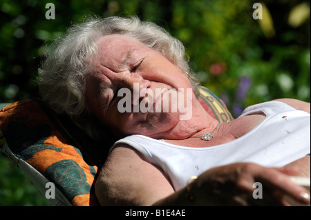 Una signora inglese titolare di pensione o di rendita gode di una posizione soleggiata giornata crogiolandovi al sole,UK,Inghilterra. Foto Stock