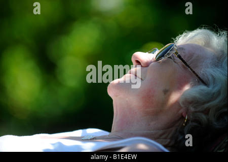 Una signora inglese titolare di pensione o di rendita OAP gode di pensionamento in una giornata di sole a prendere il sole,UK,Inghilterra. Foto Stock