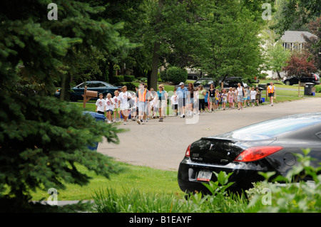 La scuola dei bambini marciando attraverso il suburban street per celebrare la fine dell anno scolastico. Foto Stock