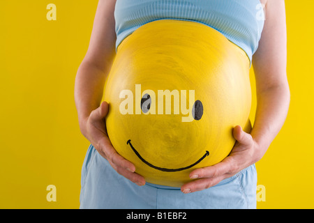 Vista della donna incinta il ventre giallo con faccina sorridente dipinta sul suo stomaco Alaska Stati Uniti Foto Stock