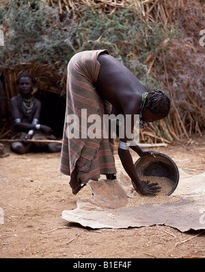 Una donna Dassanech granella winnows versando dal suo stagno metallico e lasciandolo cadere su una pelle di vitello. Foto Stock