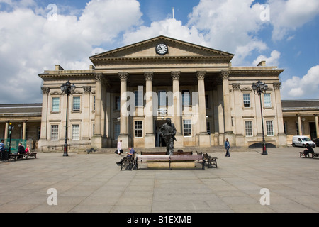 Stazione di Huddersfield con una statua del Primo Ministro Harold Wilson con un passeggero la lettura di un calendario Foto Stock