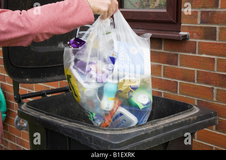 Donna mettendo il sacchetto in plastica dei rifiuti nel nero bidone con ruote al di fuori di casa. La Gran Bretagna REGNO UNITO Foto Stock