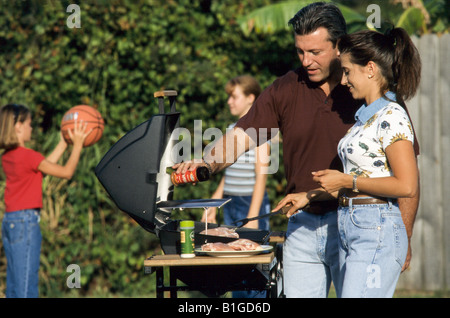 Cucina di famiglia barbeque nel cortile, con i bambini a giocare a basket Foto Stock