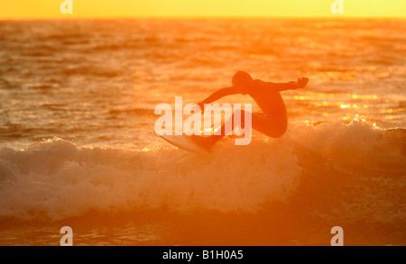 Un surfista Cavalca le onde della sera come il sole tramonta su Sennen beace in Corwall, UK. Foto Stock