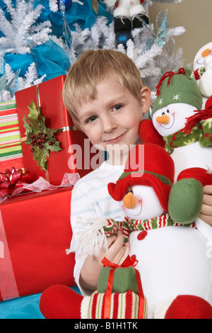 Ragazzo (5-6) azienda farcite pupazzo di neve nella parte anteriore dell'albero di Natale, ritratto Foto Stock