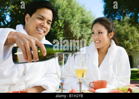 Coppia cinese indossando accappatoi, bevendo champagne al tavolo per esterno Foto Stock