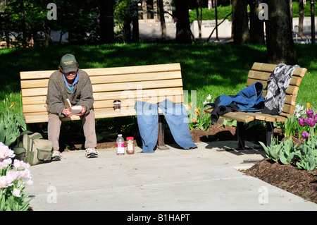 Senzatetto uomo libro di lettura su una panchina nel parco di Fort Wayne Indiana Foto Stock