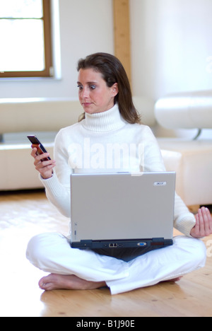 Giovane donna graziosa la pratica dello yoga con un notebook sul grembo e telefonare, seduto sul pavimento Foto Stock