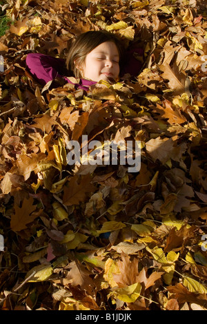 Giovane ragazza dorme sotto un mucchio di rastrellamento di foglie di quercia sotto il sole in Idaho durante l'Autunno Foto Stock