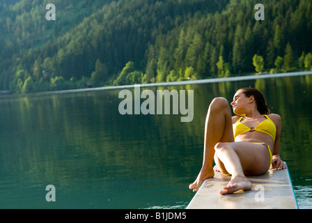 Giovane donna sdraiata su un trampolino di lancio di un lago balneabile, Austria Foto Stock