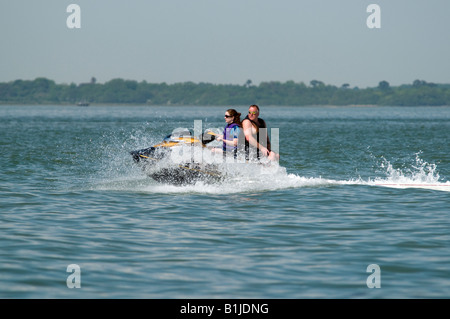 Jet bike sul mare con il bianco delle onde che si infrangono sulla battigia di fronte essendo cavalcato da due persone quello rivolto indietro Foto Stock