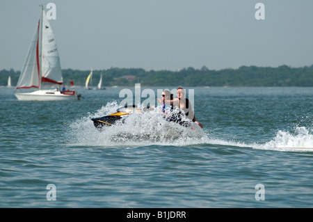 Jet bike sul mare con il bianco delle onde che si infrangono sulla battigia di fronte essendo cavalcato da due persone quello rivolto indietro Foto Stock