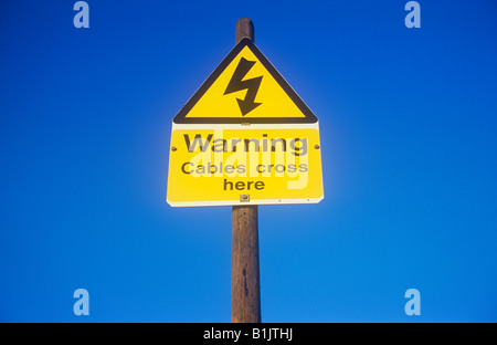 Elettricità simbolo Thunderbolt triangolare in giallo e nero a firmare la pole con il blu del cielo e le parole di avvertimento trasversale di cavi qui Foto Stock