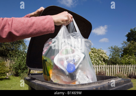 Donna mettendo il sacchetto in plastica dei rifiuti domestici in nero bidone con ruote per buttare fuori. Inghilterra Regno Unito Gran Bretagna Foto Stock