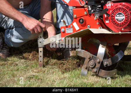 L'uomo la regolazione della profondità di scavo di un benzina rotavator giardino essendo utilizzato per il tasso di abbandono fino terreno in un giardino a Newtownabbey ir settentrionale Foto Stock