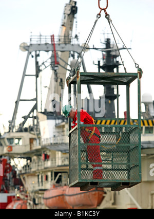 Uomo al lavoro in una gru sollevato in gabbia di sicurezza al Porto di Aberdeen, Scozia, Regno Unito Foto Stock