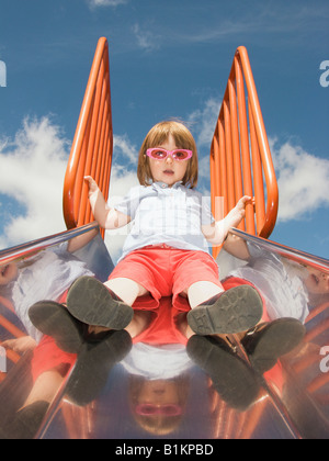 22 mese vecchia ragazza seduta nella parte superiore di una diapositiva in un parco giochi Foto Stock