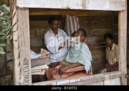 INDIA Kerala KOCHI piccolo negozio di barbiere in una baracca su una strada di sporco nella città di Kochi con il barbiere la rasatura One Customer Foto Stock