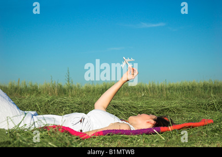 Giovane donna che giace nel campo giocando con aeroplano giocattolo Foto Stock