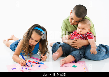 Giovane ragazza latino colorazione sulla costruzione della carta mentre fratelli guarda Foto Stock