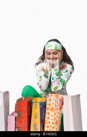 Giovane donna seduta dietro di borse per lo shopping e guardando sorpreso Foto Stock