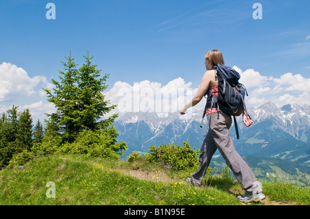Donna single passeggiate lungo il sentiero in Dientner Berge gamma con Steinernes Meer (Stone Mare) la gamma della montagna di background, Austria Foto Stock