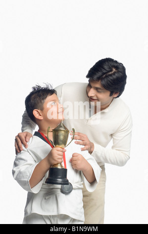 Ragazzo tenendo un trofeo e guardando suo padre Foto Stock