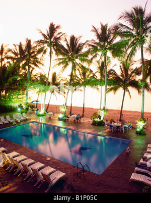 Piscina tropicale del resort con palme durante un vibrante tramonto Foto Stock