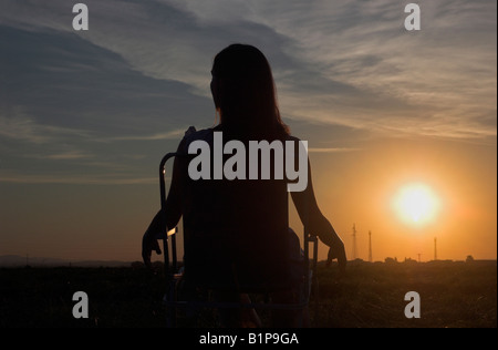 Silhouette di donna giovane seduti all'aperto in cattedra godendo bel tramonto Foto Stock