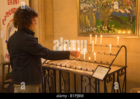 Una donna di preghiera di illuminazione candele in una chiesa Foto Stock