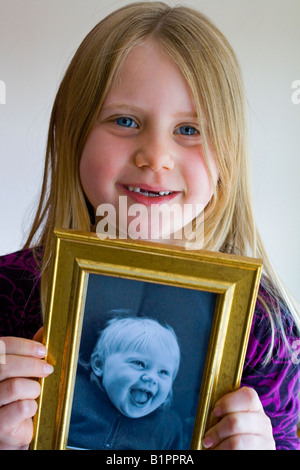 7 anno vecchia ragazza tenendo un immagine di se stessa come un bambino che mostra lo sviluppo infantile Foto Stock