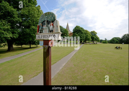 Il segno di villaggio in villaggio a Alfriston verde (noto localmente come La Tye) con St Andrews chiesa in background. East Sussex, Regno Unito. Foto Stock