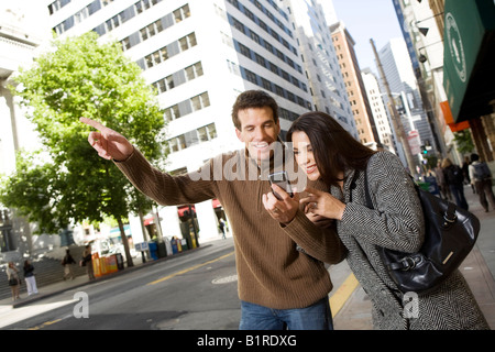 Una giovane coppia sono passeggiando sotto braccio attraverso un centro di zona della città portando un dispositivo tenuto manualmente. Foto Stock
